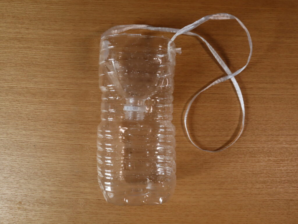 Photograph of a plastic bottle trap used for bottle fishing, complete with string to secure it to a point.